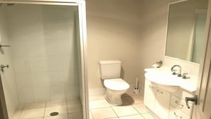 A bathroom with a toilet, sink, mirror, and shower area. - Coastal Escape (Tura Beach)
