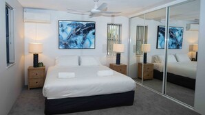 A modern bedroom with a large bed, two bedside tables with lamps, a ceiling fan, and abstract artwork on the walls. - Byron Bay Accom - Nautilus 1 - 46 Lawson Street (Byron Shire)