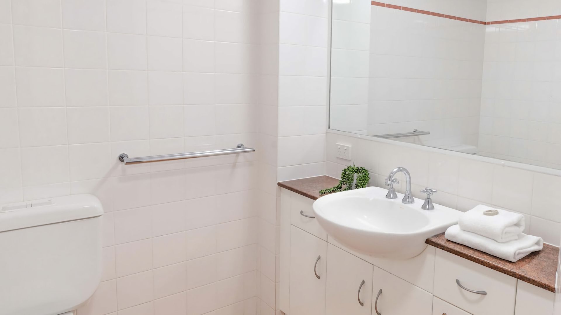 Un baño con inodoro blanco, un lavamanos con espejo y una toalla sobre la encimera.