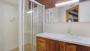 Ein Badezimmer mit Duschkabine aus Glas, einem weißen Waschbecken, Holzschränken und einem Spiegel über dem Waschbecken.