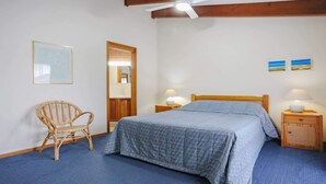 Quarto com cama, poltrona, mesa de cabeceira e ventoinha no teto.