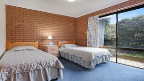 Ein Schlafzimmer mit zwei Betten, einer Ziegelwand, einem Fenster mit Vorhängen und einem blauen Teppich.