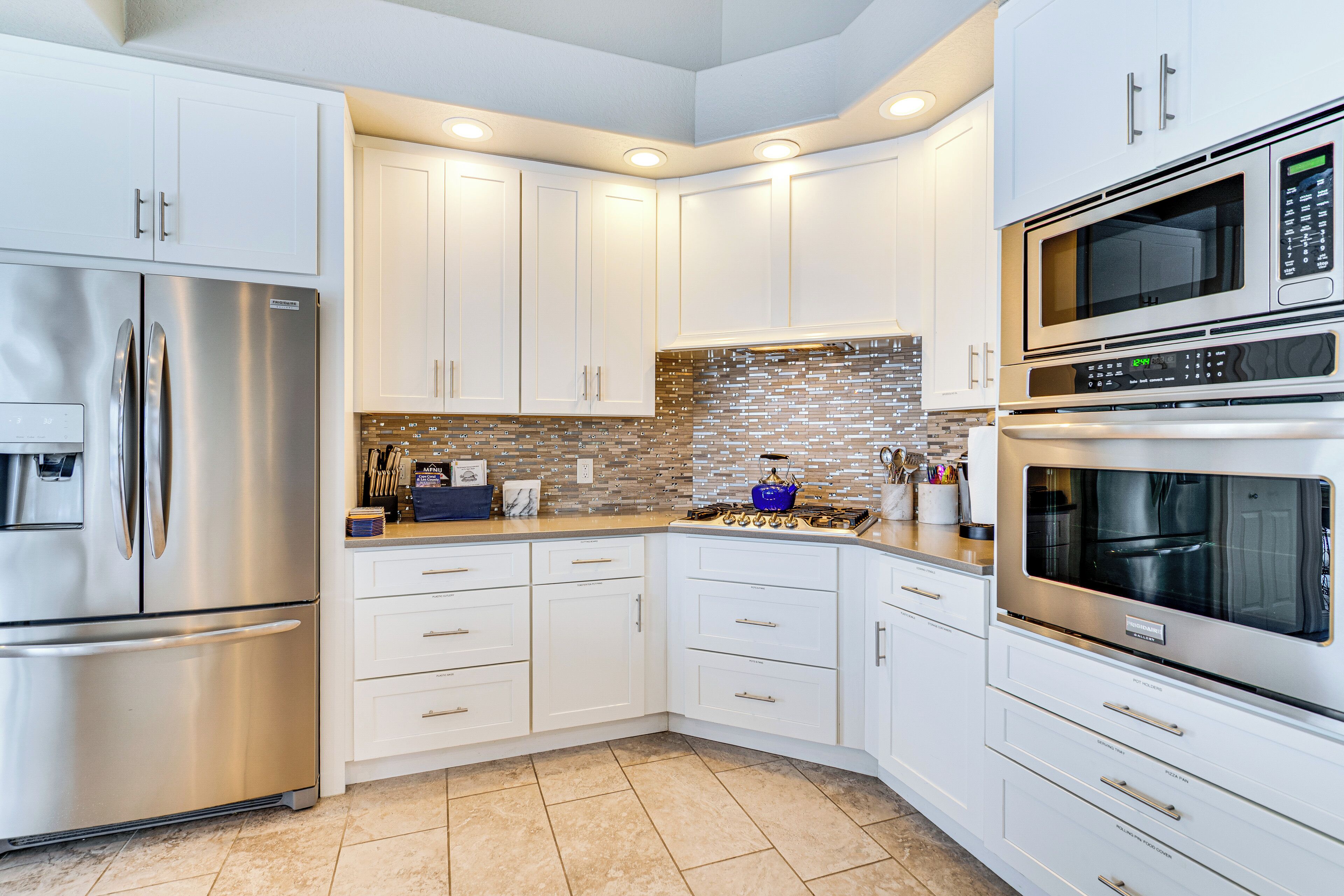 A modern kitchen with white cabinets, stainless steel appliances, and a tiled backsplash.