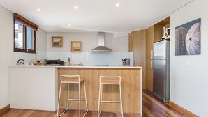 Uma cozinha moderna com uma ilha central, banquetas de madeira, uma geladeira de aço inoxidável e armários de madeira.