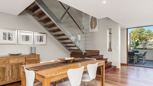 Uma cozinha moderna com armários de madeira, uma mesa de jantar com cadeiras e uma escada com guarda-corpo de vidro.
