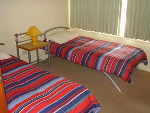 A room with two beds, a small table with a lamp, and a window with curtains. - Deja Blue - Pambula Beach (Pambula Beach)