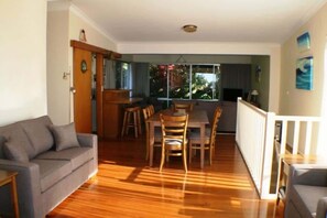 A living room with a sofa, dining table, chairs, and a view through a large window.