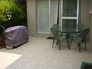A patio with a covered table and chairs, a sliding glass door, and a tiled floor.