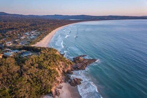 Vista aérea de una zona costera con playa, zona boscosa y edificios dispersos.