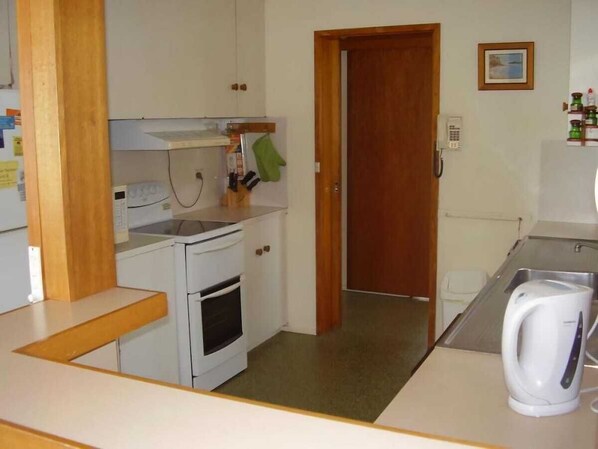 Una cocina compacta con armarios blancos, estufa, fregadero y hervidor.