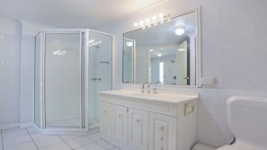 A bathroom with a glass shower enclosure, a white sink with a mirror above it, and a toilet. - Quarterdeck 3 (Tura Beach)
