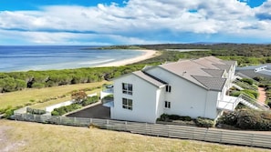 Un bâtiment moderne, de couleur blanche, doté d’un toit plat et situé près d’une plage, offrant une vue dégagée sur l’océan.