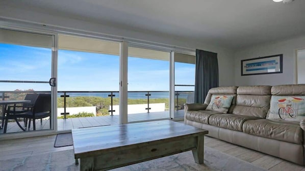 Un salon comprenant un canapé, une table basse et une vue sur la mer, grâce à de grandes portes-fenêtres coulissantes.
