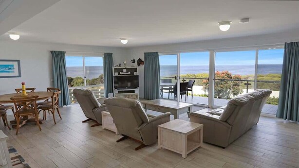 Een ruime woonkamer met een grote schuifpui naar een balkon met uitzicht op de oceaan.