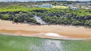 An aerial view of a coastal property with a beach, a stream, and a cluster of houses. - Quarterdeck 3 (Tura Beach)