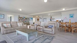 Een ruime woonkamer met een zithoek, een salontafel en een eethoek met houten stoelen en een tafel.