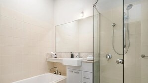 Ein modernes Badezimmer mit einer Duschkabine, einer weißen Badewanne und einem Waschtisch inklusive Spiegel und Waschbecken.