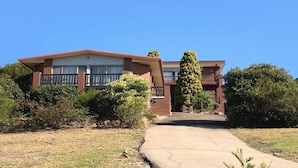 A two-story house with a front porch, a brick facade, and a small front yard with shrubs and a tree.