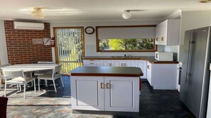 Une cuisine avec des meubles blancs, un plan de travail en bois, un réfrigérateur et un coin repas comprenant une table et des chaises.