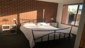 A bedroom with a brick wall, a bed with a metal frame, bedside tables, and a window.