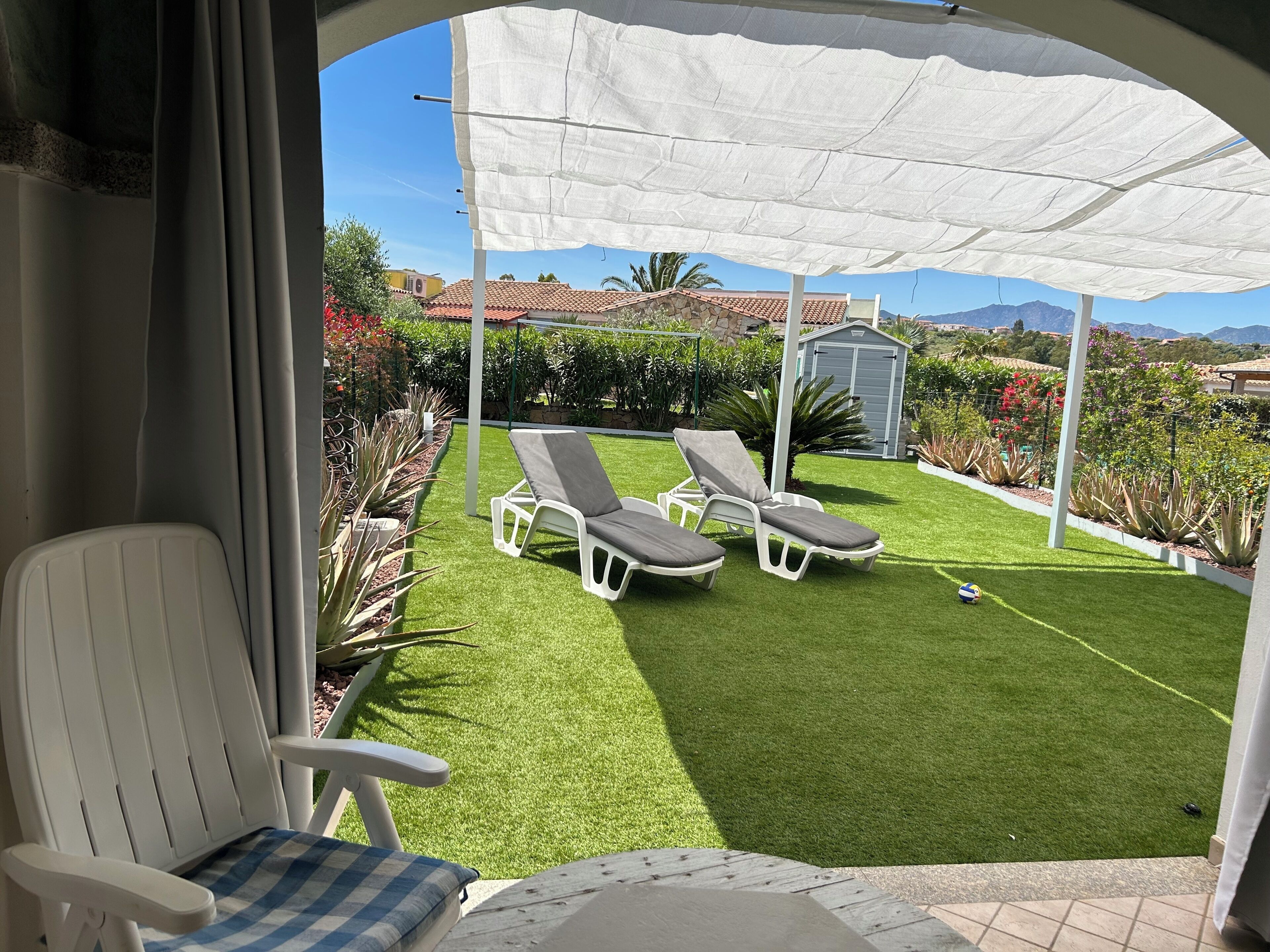 A patio with two white lounge chairs, a white umbrella, and a small shed in the background.
