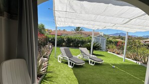 A patio with two white lounge chairs, a white umbrella, and a small shed in the background. - Budoni Villetta EDDY between sea and nature (budoni)