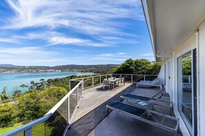 A balcony with a view of the sea, a dining area, and a glass table.
