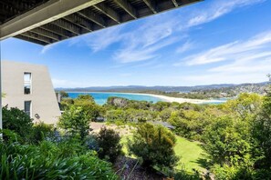 A modern building with a view of a coastal landscape, including a beach and distant hills.