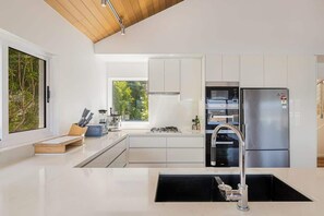 A modern kitchen with white cabinetry, stainless steel appliances, and a large window providing natural light.
