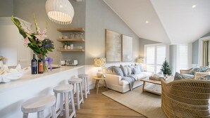 Eine moderne Küche mit weißen Barhocker, einem weißen Sofa und einem Korbstuhl.