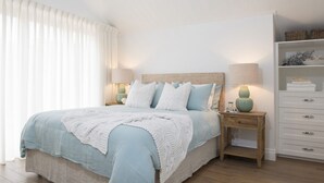 Ein Schlafzimmer mit Bett, Nachttischen, einem Schminktisch und einem Fenster mit Vorhängen.