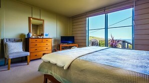 A bedroom with a bed, dresser, TV, and a large window with a view. - Bantry Two (Merimbula)