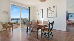A room with a dining table, chairs, a large window with a view, and artwork on the walls.