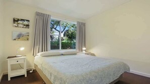 A bedroom with a bed, two bedside tables, a window with curtains, and wall-mounted artwork.