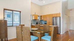 Una cocina moderna con armarios de madera, un refrigerador de acero inoxidable y un comedor con sillas de mimbre y cojines azules.