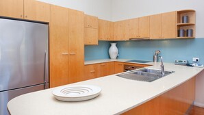 Una cocina moderna con armarios de madera, un refrigerador de acero inoxidable, un lavamanos y una encimera blanca.