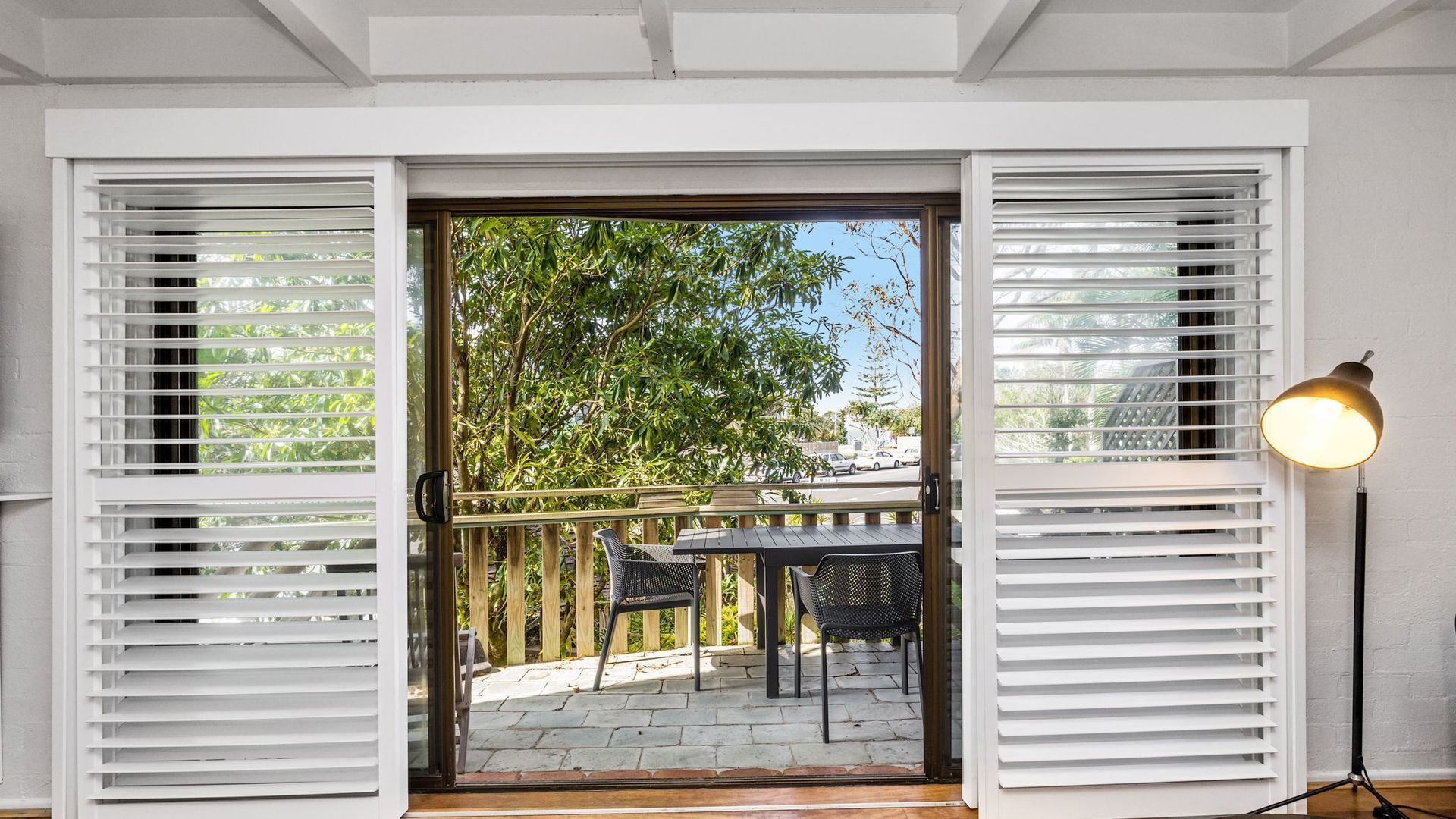 A doorway with white shutters, a patio with a table and chairs, and a lamp on the right.