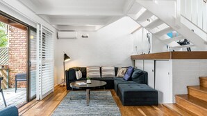 A modern living room with a sectional sofa, a coffee table, and a staircase. - Byron Bay Accom - Balcony on Lawson - 6 - 34 Lawson Street (Byron Shire)