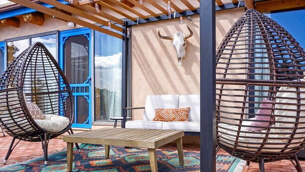 Een terras met twee hangstoelen, een houten tafel en een witte bank.