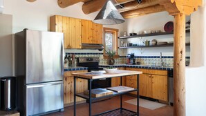 Een keuken met houten kastjes, een roestvrijstalen koelkast, een zwart fornuis en een hangende lamp.