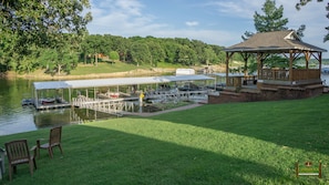 A lakeside gazebo with a covered dock area, boats, and a grassy lawn.