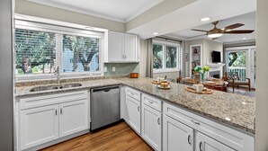 A modern kitchen with white cabinets, granite countertops, a dishwasher, and a dining area with a table and chairs. - GREAT Central Resort Location! Walk to Amenities! Community Pool! (Isle Of Palms)
