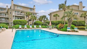 A swimming pool with lounge chairs and umbrellas, surrounded by palm trees and a multi-story building. - GREAT Central Resort Location! Walk to Amenities! Community Pool! (Isle Of Palms)