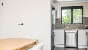 A modern kitchen with stainless steel appliances, a window with a view of greenery, and a white dining area. - Byron Bay Accom - Summer Central - Apartment 3  - 5-9 Somerset Street (Byron Shire)