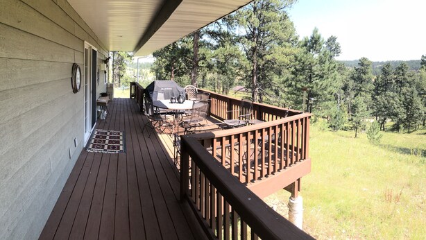 A wooden deck with a table and chairs, a grill, and a view of a forested area. - High Pines Hideaway  on Two Bit Springs Rd. (Deadwood)