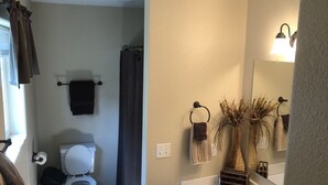 A bathroom with a toilet, sink, and shower. There are towels hanging on the wall and a mirror above the sink. - High Pines Hideaway  on Two Bit Springs Rd. (Deadwood)