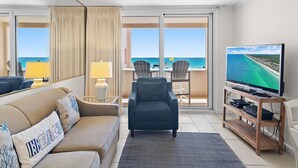Ett hotellrum med en soffa, fåtölj, TV och utsikt över havet.