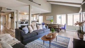A spacious living room with a dark blue sofa, a coffee table, and a patterned rug. There is a dining area with a table and chairs, and a kitchen in the background. - 4 Outdoor Areas * A/C * 5 Parking * 3 Levels * Dog OK (San Diego)