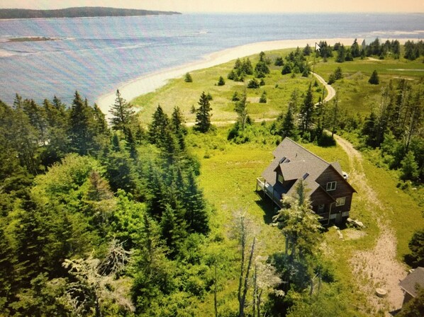 A house surrounded by dense forest and a curved shoreline.