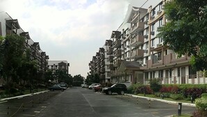 Rua residencial com edifícios de apartamentos de ambos os lados, carros estacionados e árvores.